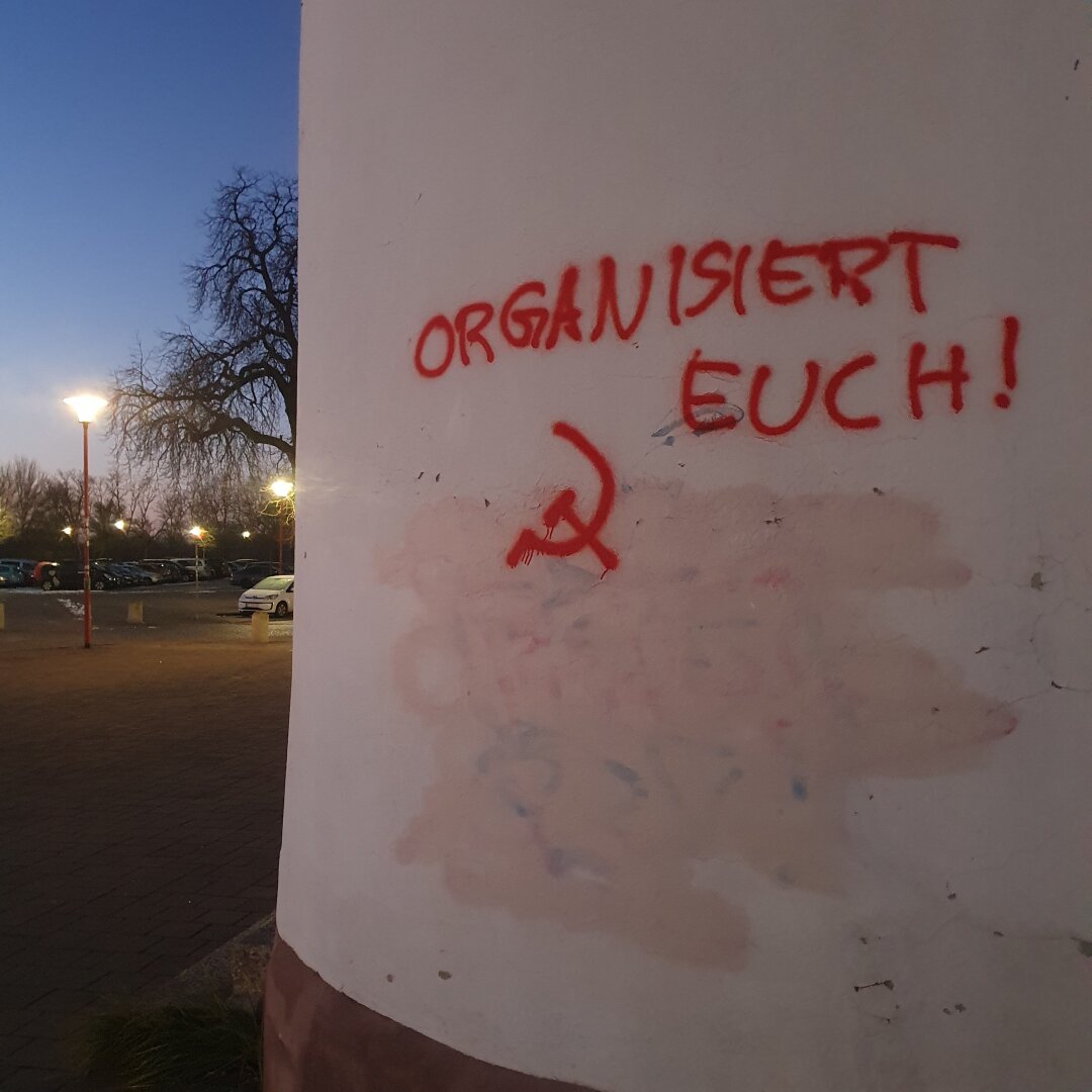 Sprayed graffiti says organisieren euch with hammer and sickle. On side of a building, early winter morning.
