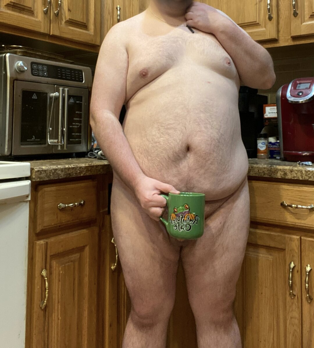 Silain standing naked while holding a mug covering his privates