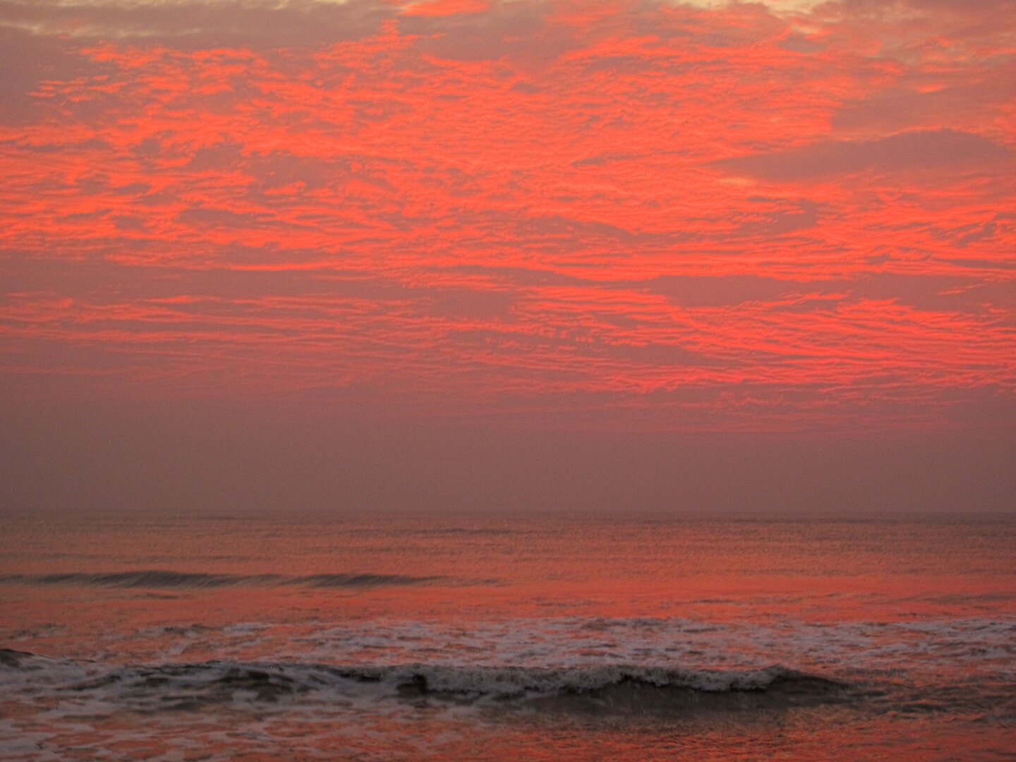 Red sky at dawn over the sea at Aleenta, Pranburi, Thailand, with gentle waves reflecting the vivid crimson and orange hues of the clouds.