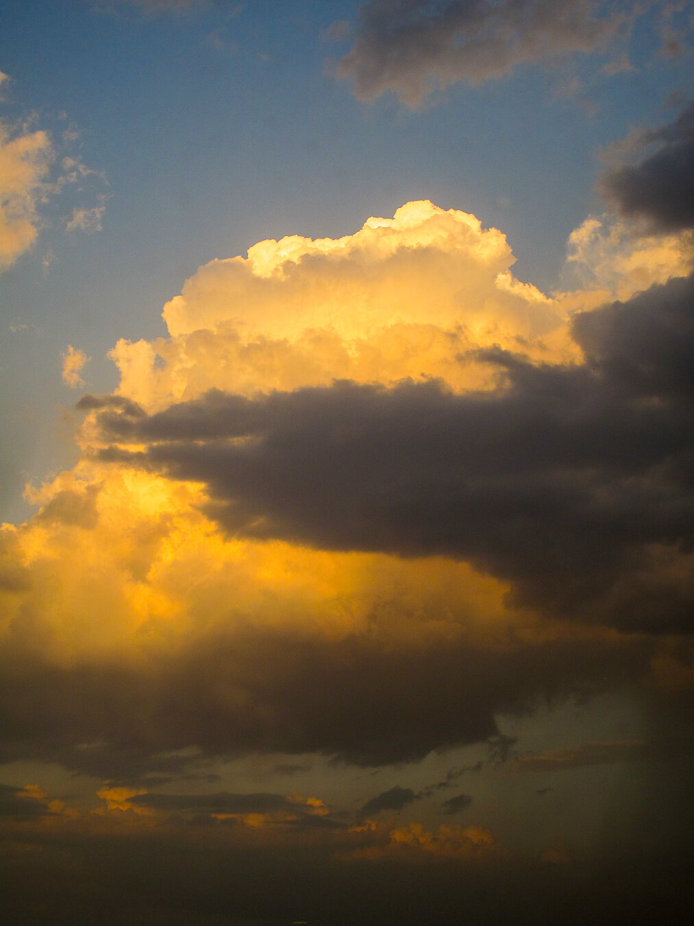 Towering monsoon clouds over Islamabad, Pakistan, illuminated by golden evening light. The upper cloud tops glow warmly against a deepening blue sky, while darker storm layers drift below, creating a dramatic contrast of light and shadow that captures the power and beauty of seasonal weather.