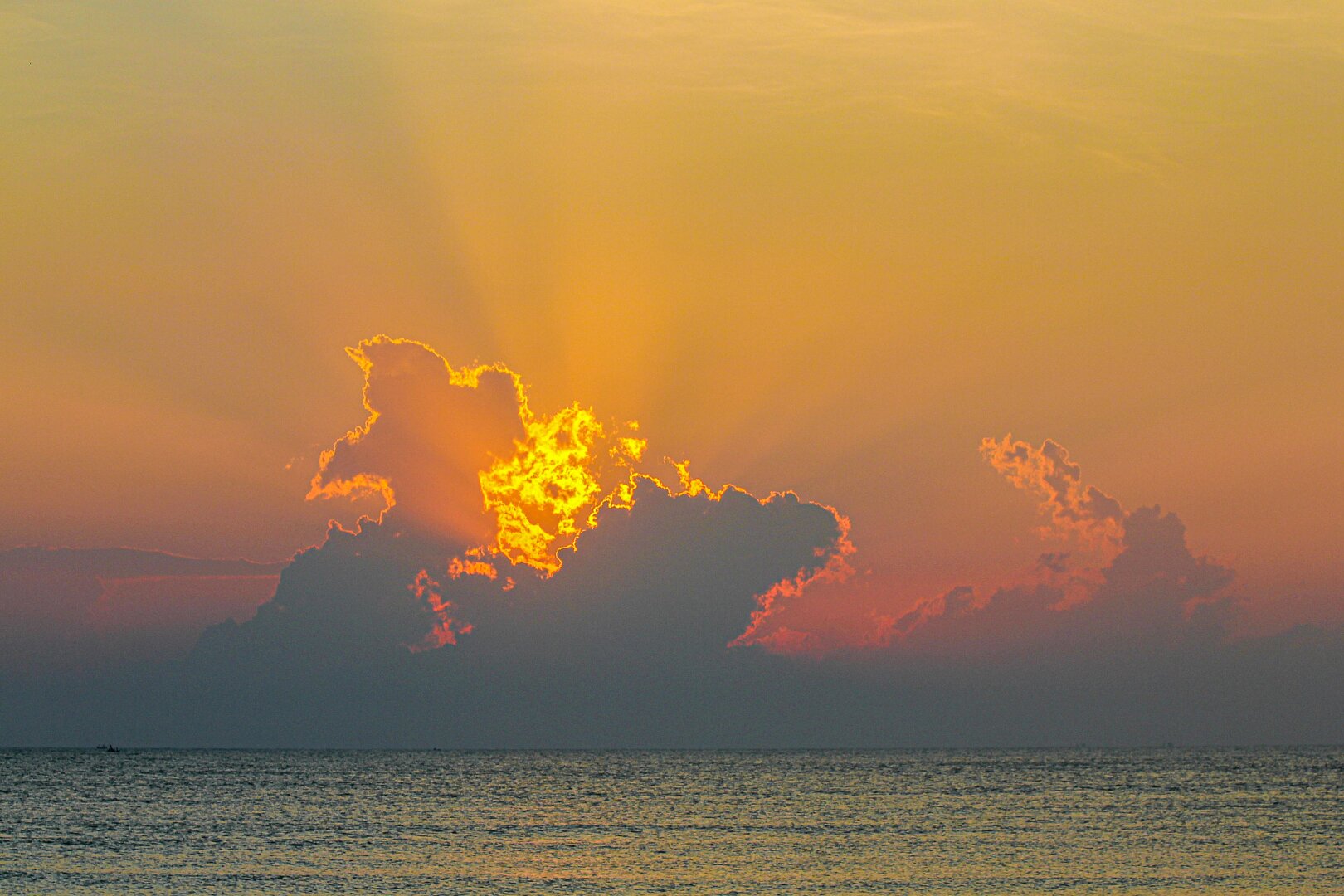Golden light breaks through dark clouds over the Gulf of Thailand at sunrise, casting warm rays across the calm sea.