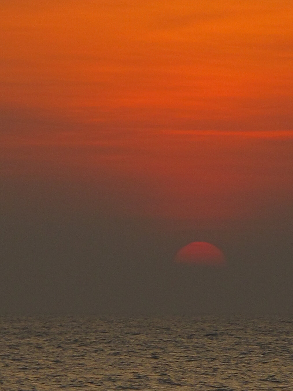 A deep orange sky over the sea at dawn, with the sun half‑visible above the horizon casting warm light across calm water at Aleenta, Pranburi, Thailand.
