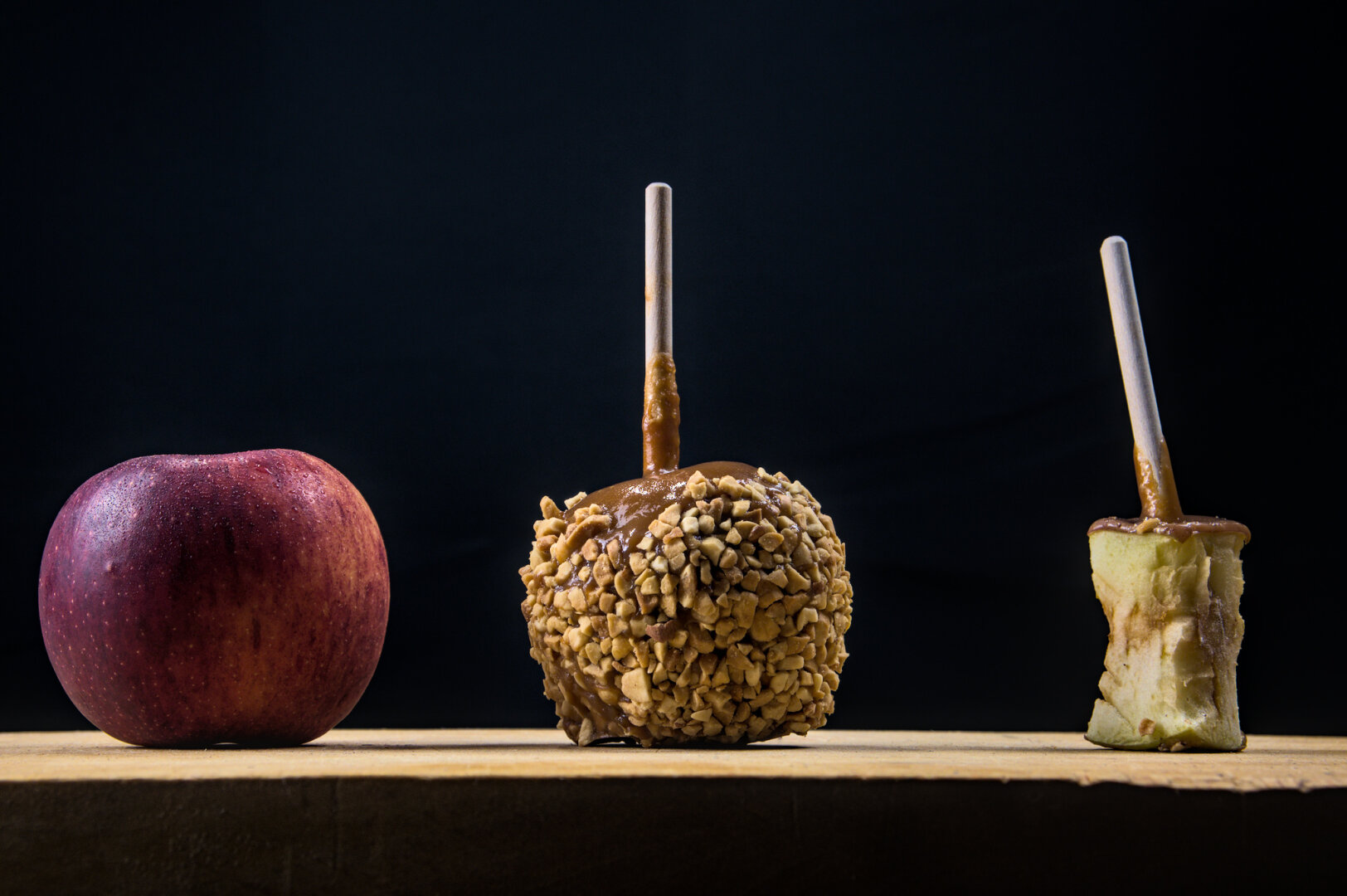 A fresh apple, a caramel apple, and a caramel apple with only the apple core and stick left.
