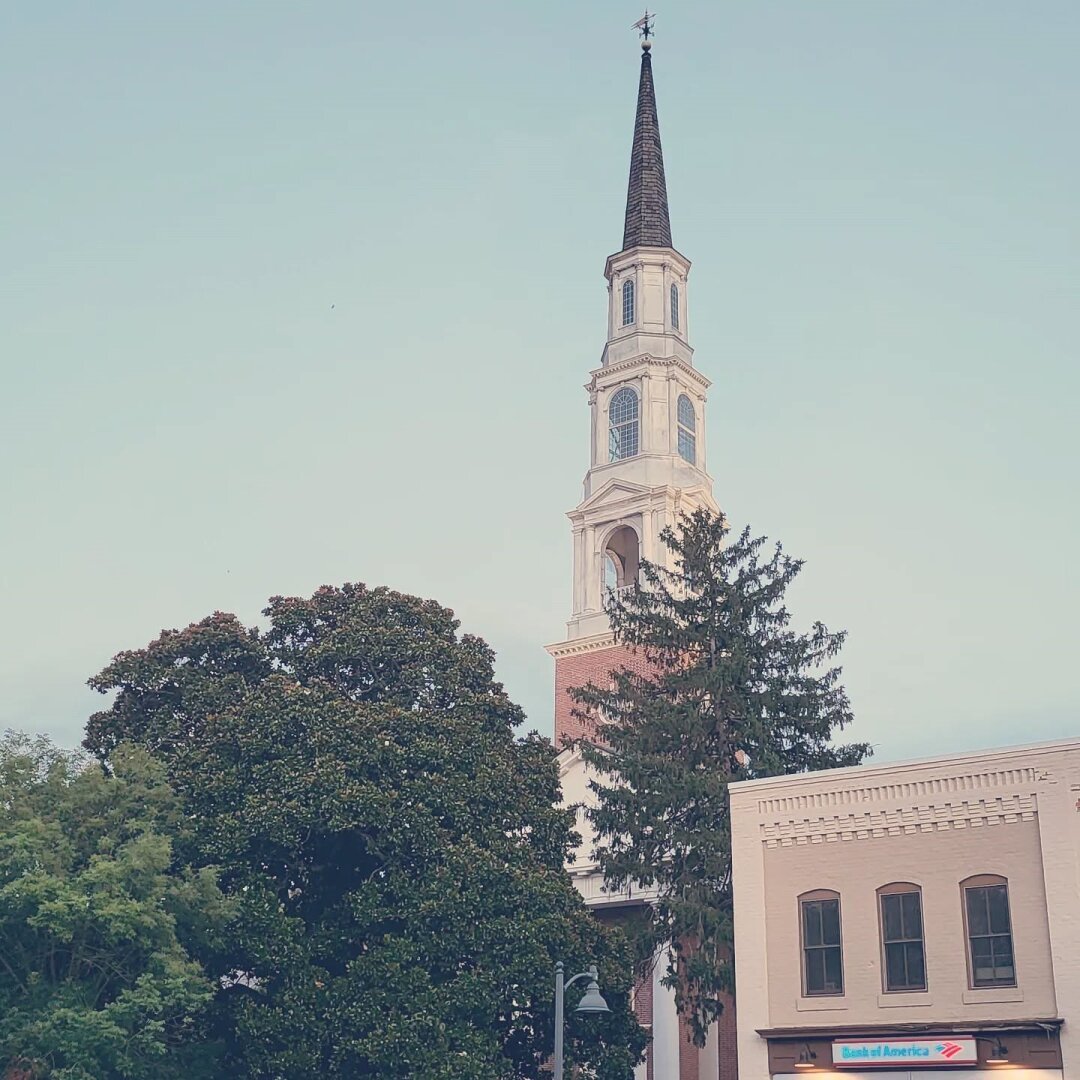 View of a church steeple rising above a treeline into the blue sky