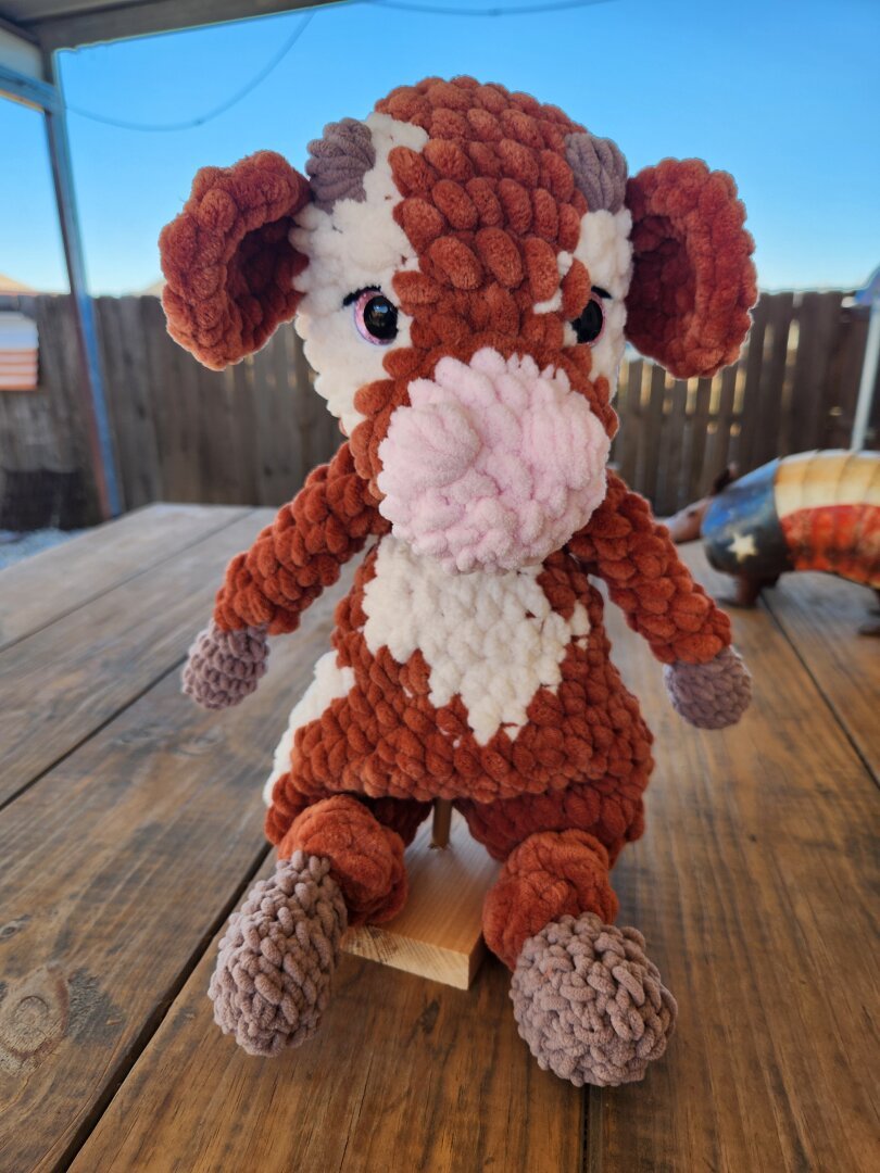 Crochet reddish brown cow with cream colored spots in a sitting position, wooden table