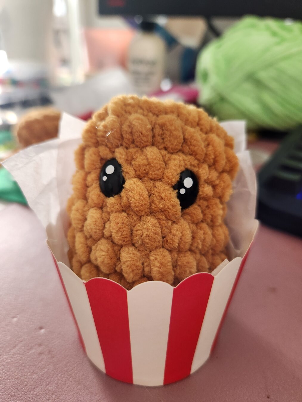 Crochet chicken nugget with golden colored yarn sitting in a red and white striped cup for presentation for craft fair.