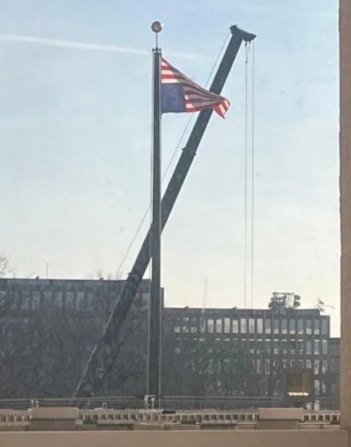 A large American flag flying upside down in front of a large building