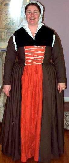 I am wearing a brown overdress, split to show a pumpkin orange underdress, laced at the center bodice and a white linen cap