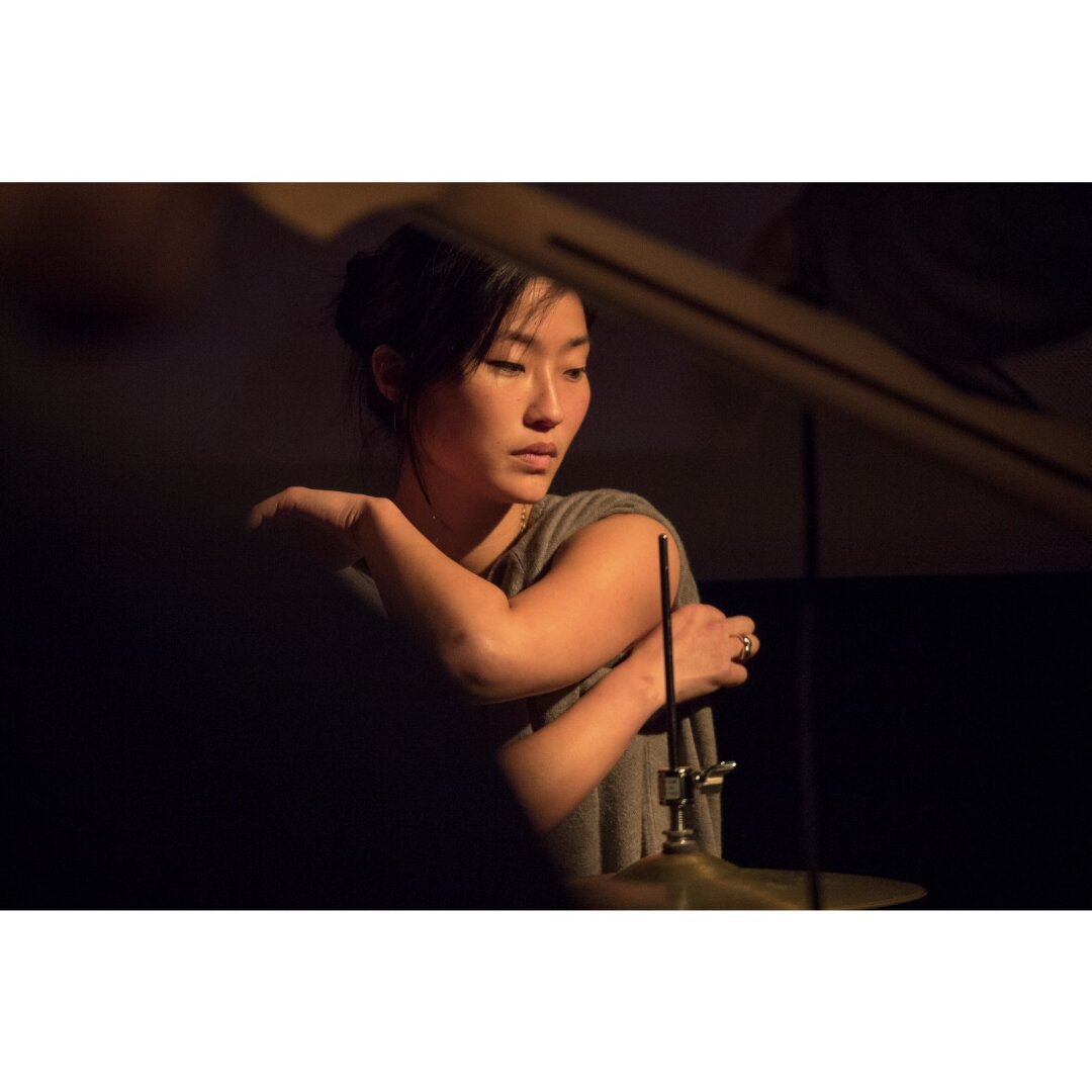 Tiffy Yoon, the drummer for Amanda X, framed by the neck of a bass and her drum kit, between songs.