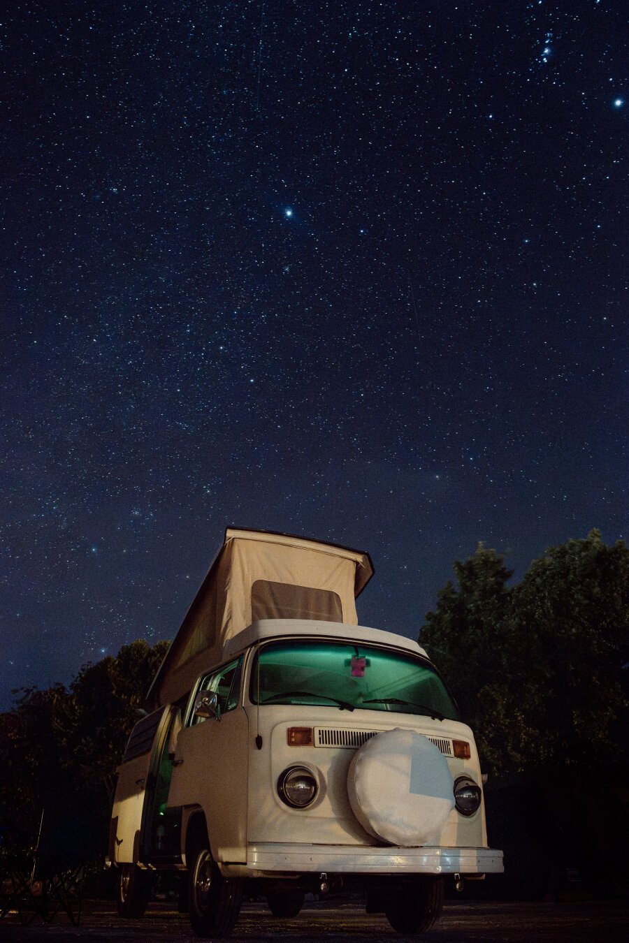 A long exposure of the night sky with an old Volkswagen camper bus in the foreground.