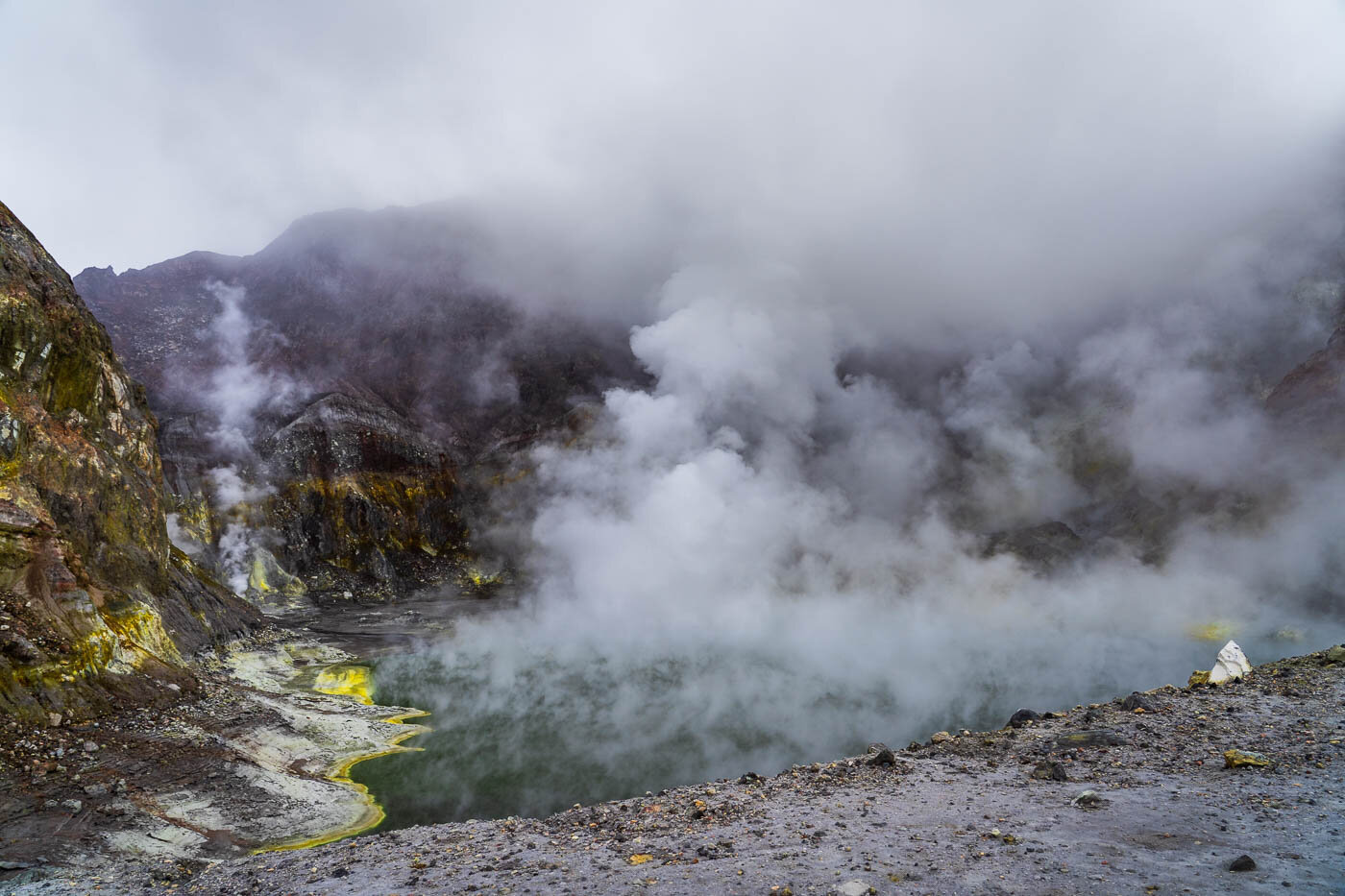 Wide-angle view of White Island’s volcanic crater, with thick steam rising from the crater lake under a cloudy sky.