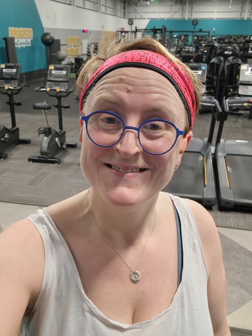 Photo of Ruth in a white vest top on a treadmill in a gym. She's wearing glasses and a pink headband.