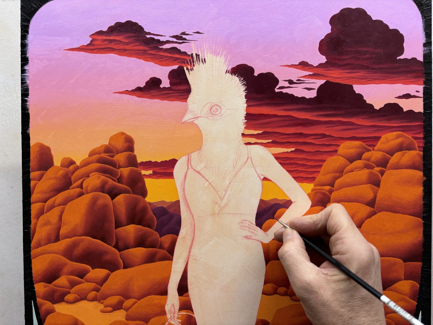 Oil painting in progress of a woman with a bird head, with sunset clouds over desert rocks and mountains in background