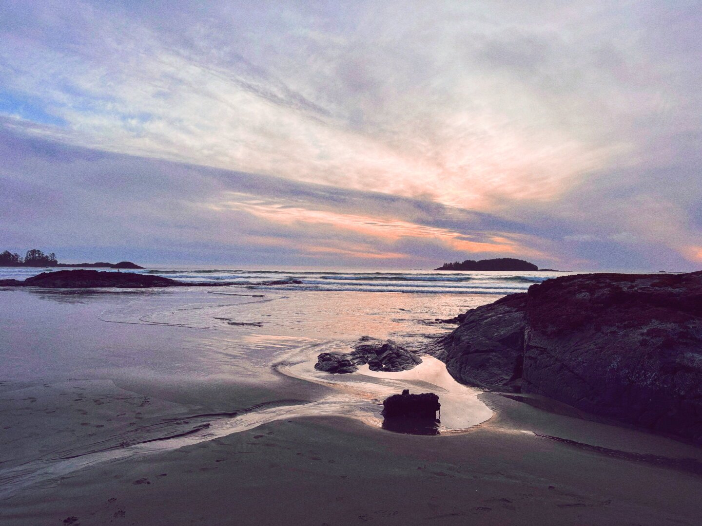 Image of a sunset looking west of Tofino at Chesterman Beach. Sky has light cloud cover and the golden hour is breaking through it gently.