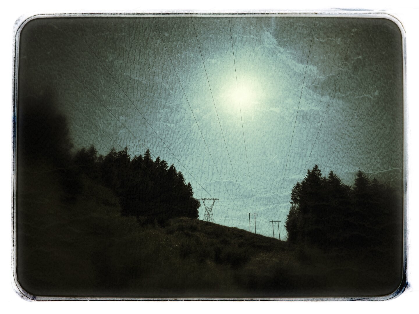 Heavily processed image of the sun high in the sky above a powering cut through the mountains.