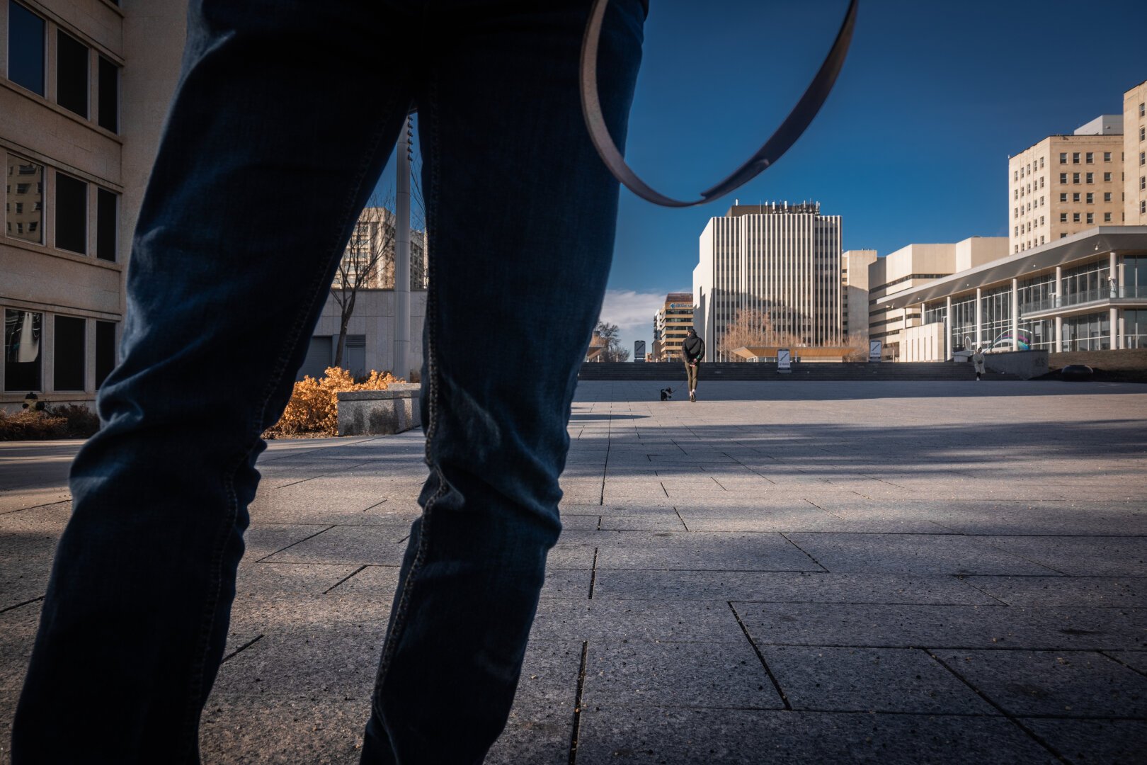 A strange juxtaposition of someone’s jeans, while worn, and an empty city square.