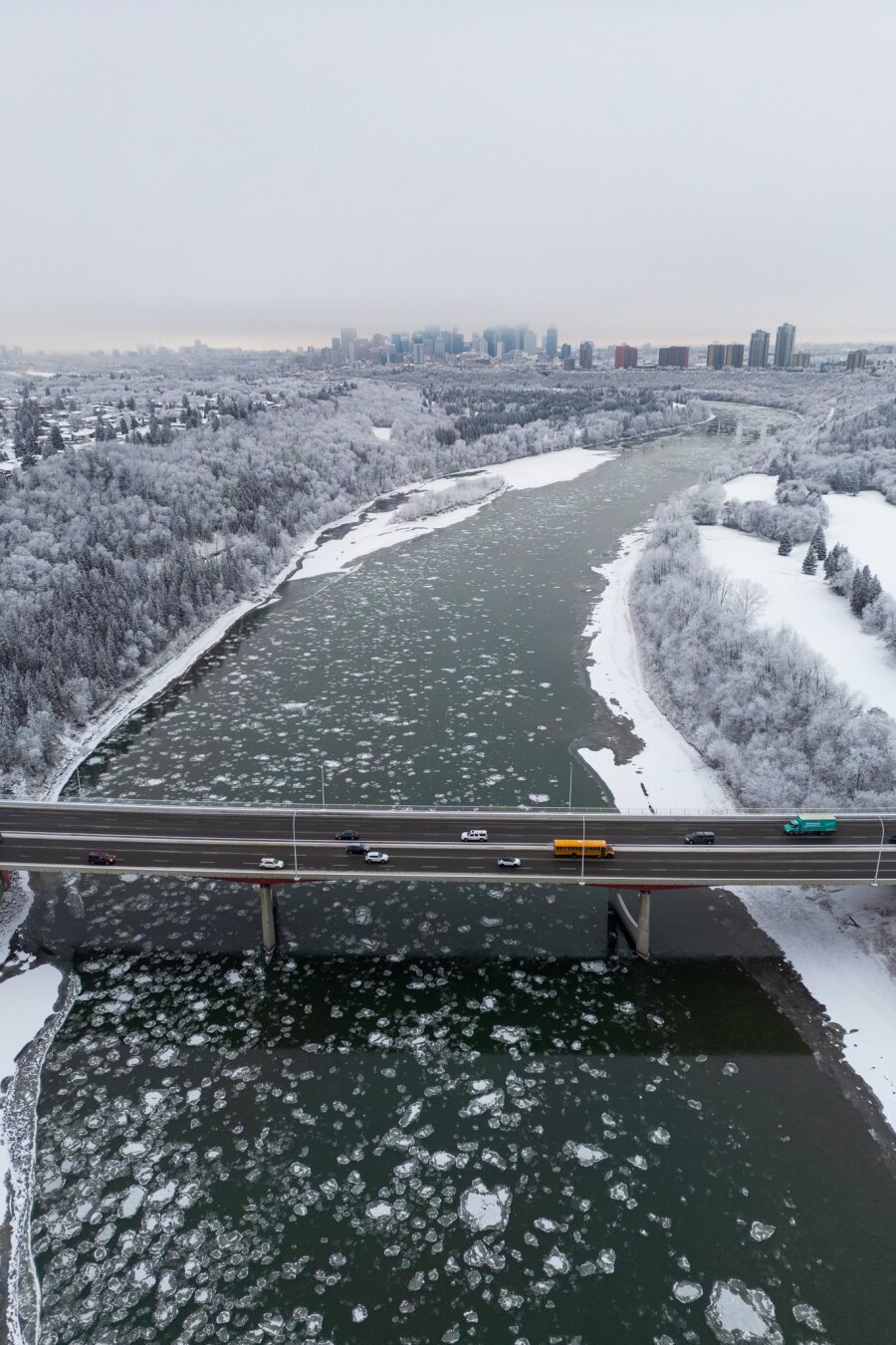 An Ariel shot of a bridge with traffic going across, with downtown Edmonton in the background. The area is covered on hoar frost.