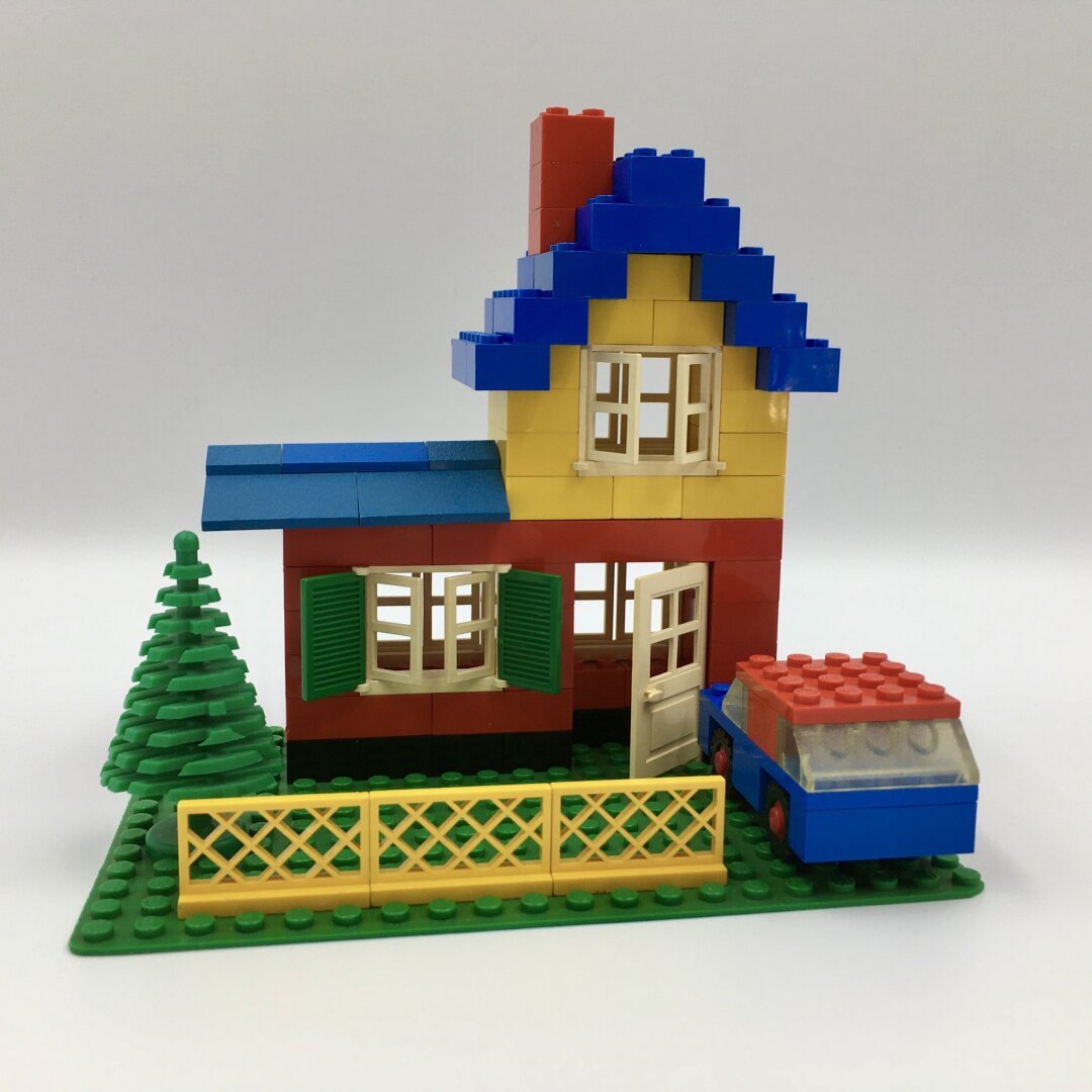 Vintage lego set. Red and yellow house with blue roof. With a little car and tree in front.