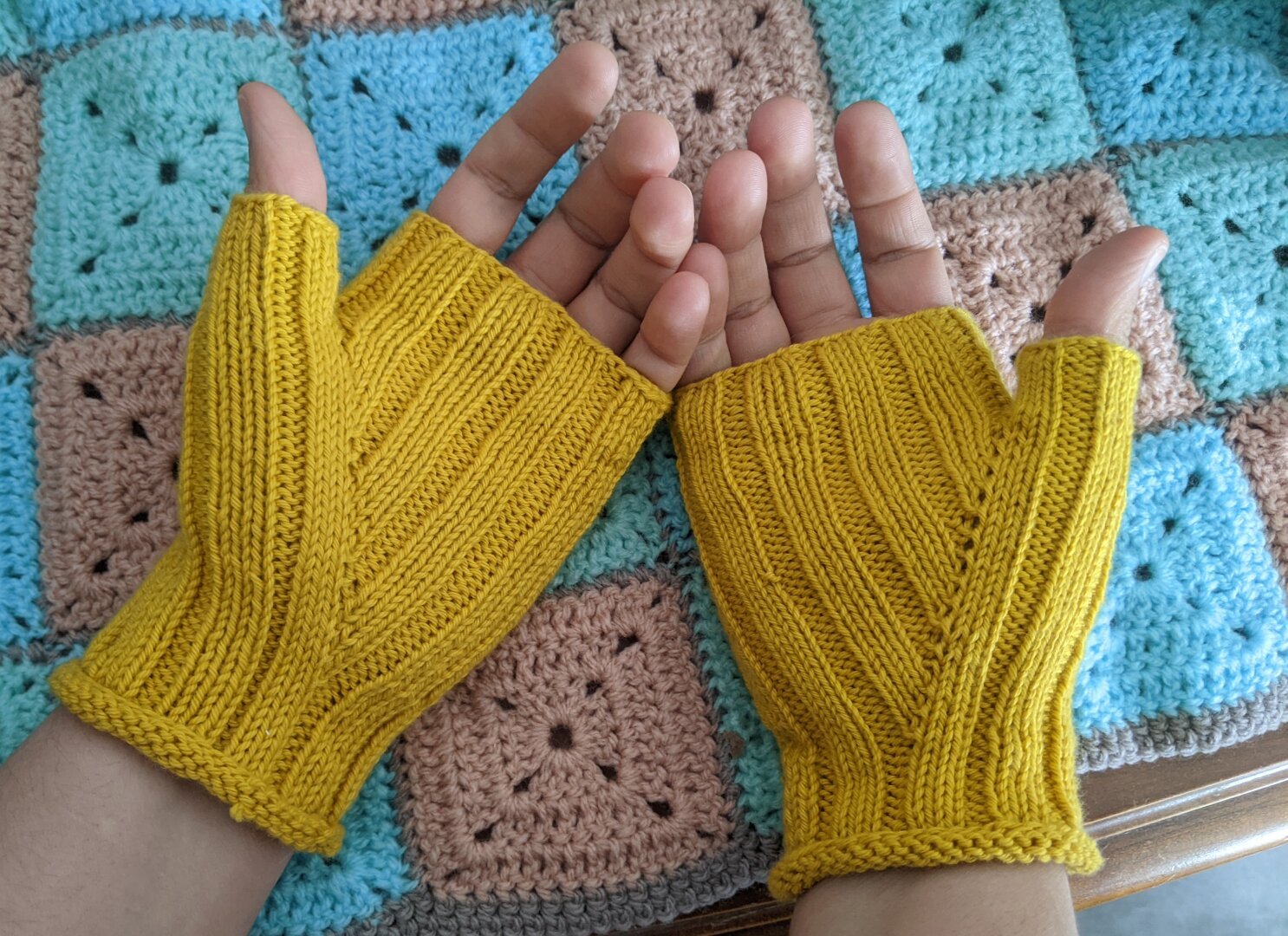 Fingerless knitted gloves in yellow cotton. The gloves are entirely in a 3x2 ribbing pattern so they have long stripes along them.