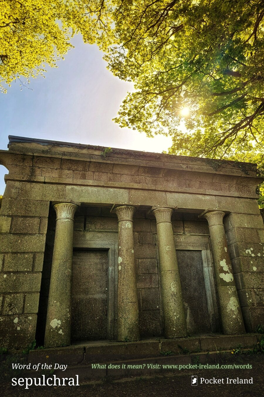 A low-angle shot of a weathered stone mausoleum constructed with monumental granite ashlar blocks and four lichen-encrusted columns. The tomb structure features recessed stone portals beneath a heavy classical entablature. Above, lush green leaves form a vibrant canopy against a pale sky, where bright golden sunlight flares through the branches over the mossy roof.