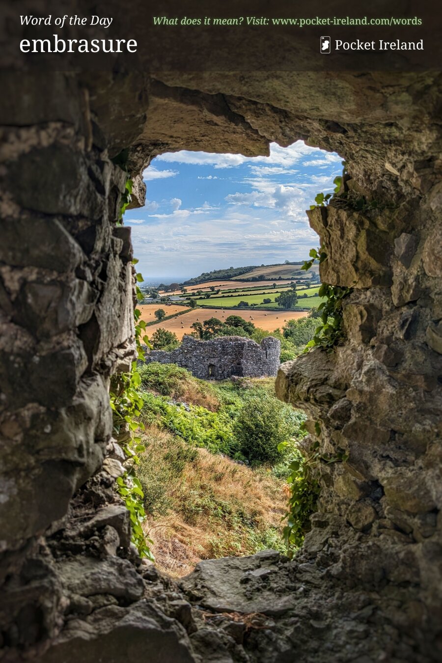 A rugged, irregular opening in an ancient stone wall frames a sunlit countryside vista. Rough, mortar-flecked grey stones and clinging green ivy surround the aperture in deep shadow. Through the opening, rolling emerald and golden-yellow agricultural fields stretch beneath a bright blue sky dotted with soft white clouds, overlooking a lower stone ruin nestled among lush greenery on the sunlit hillside.