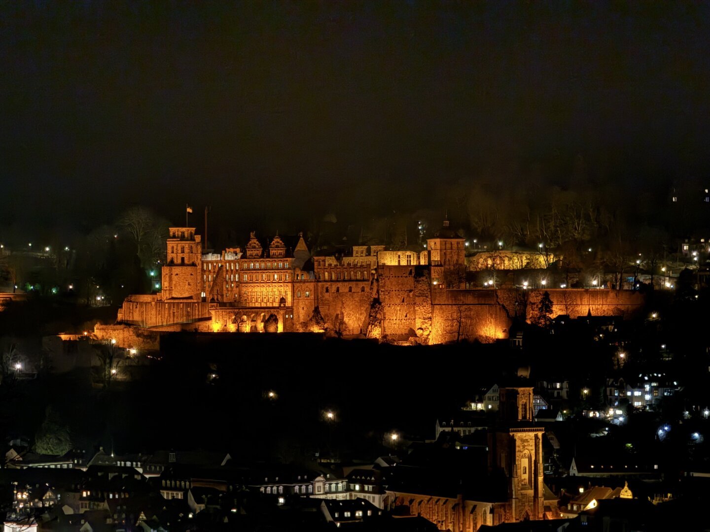 Das beleuchtete Heidelberger Schloss vom Philosophenweg aus bei Nacht.