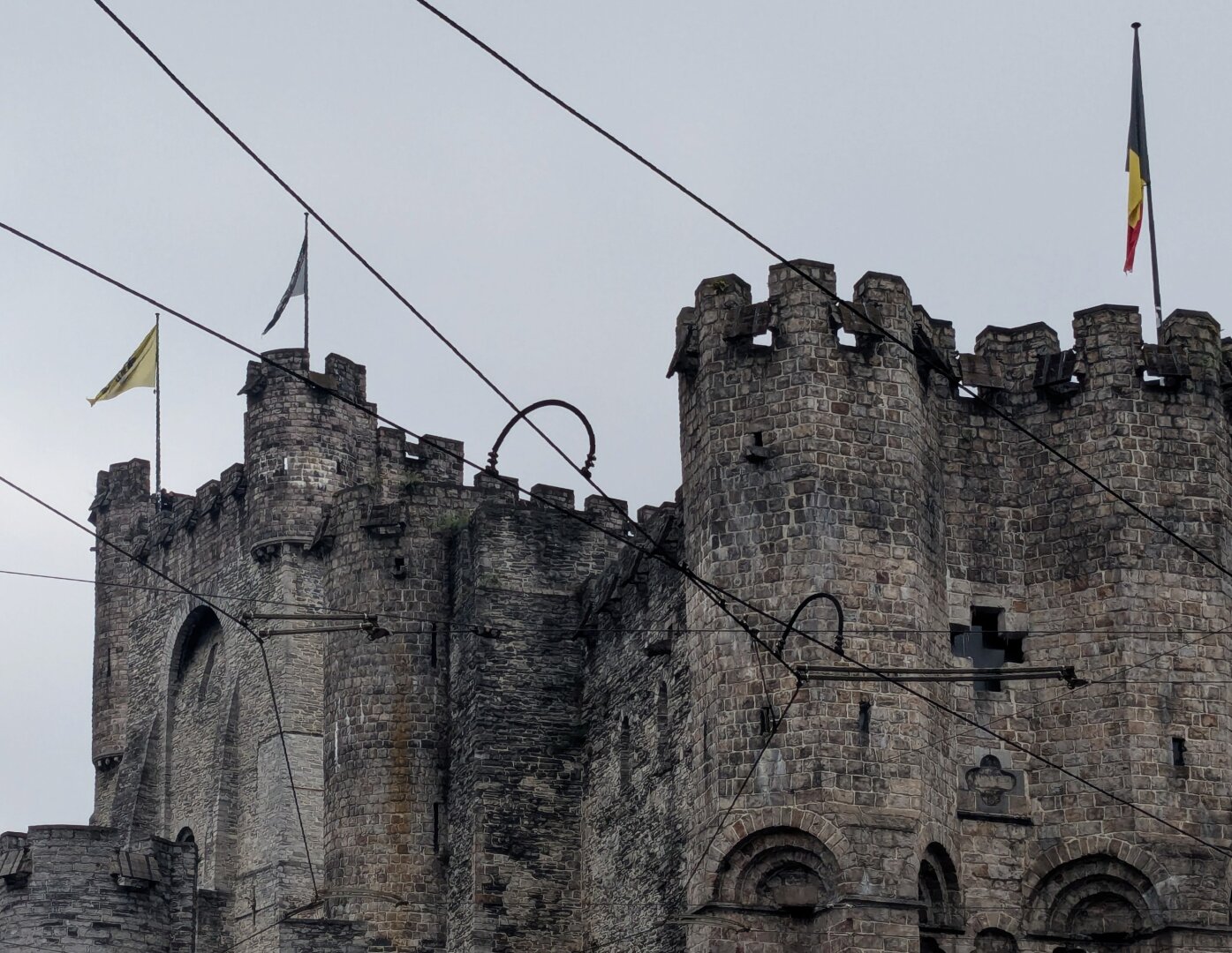 Upper body of medieval stone castle with Belgian flags