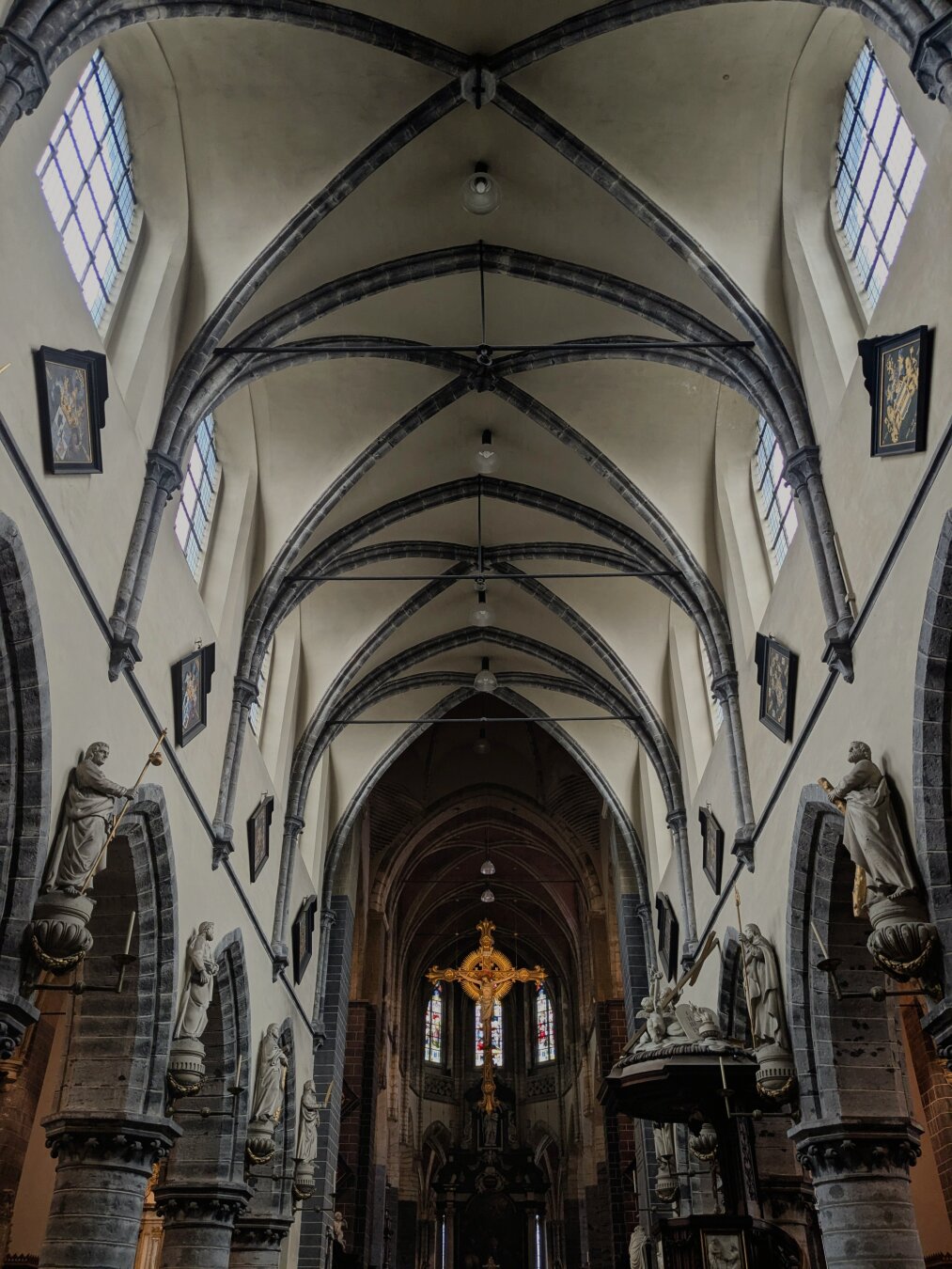 Interior of gothic church with white and grey rib vaults and golden crucifix at the end of the nave