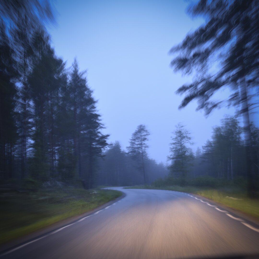 Blurry night pic of a road, bluish light with head lights from the car closest to the camera