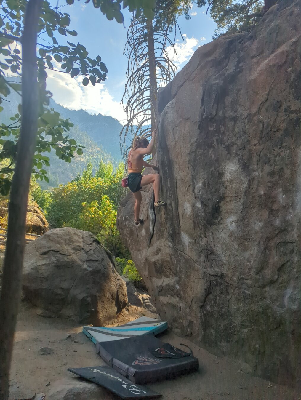A woman most of the way up a bouldering problem with mountains in the background