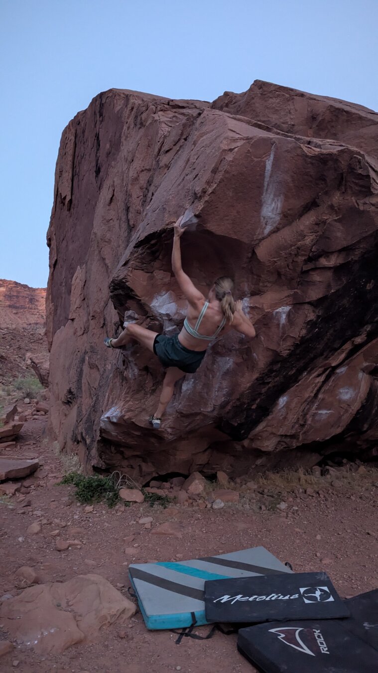 A climber on a large overhung corner of a boulder.