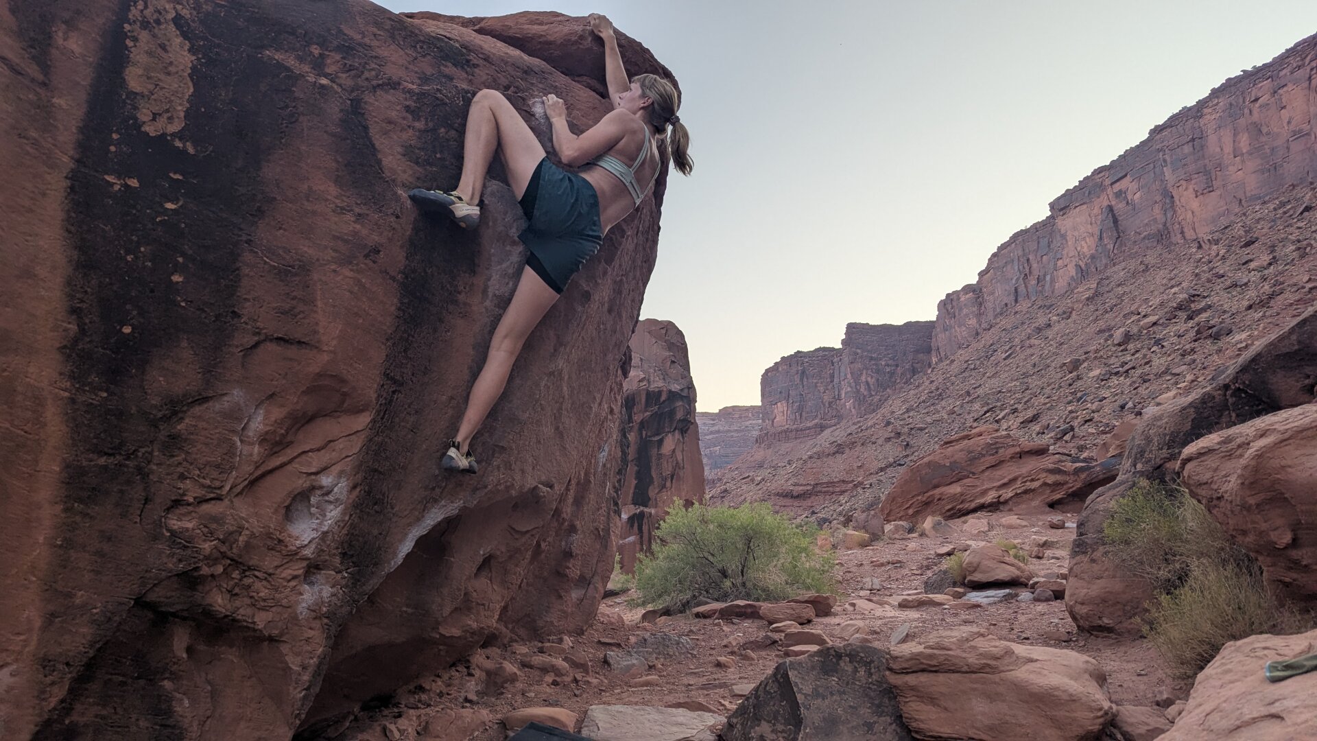 A climber reaching the top of a boulder with canyon walls in the background.