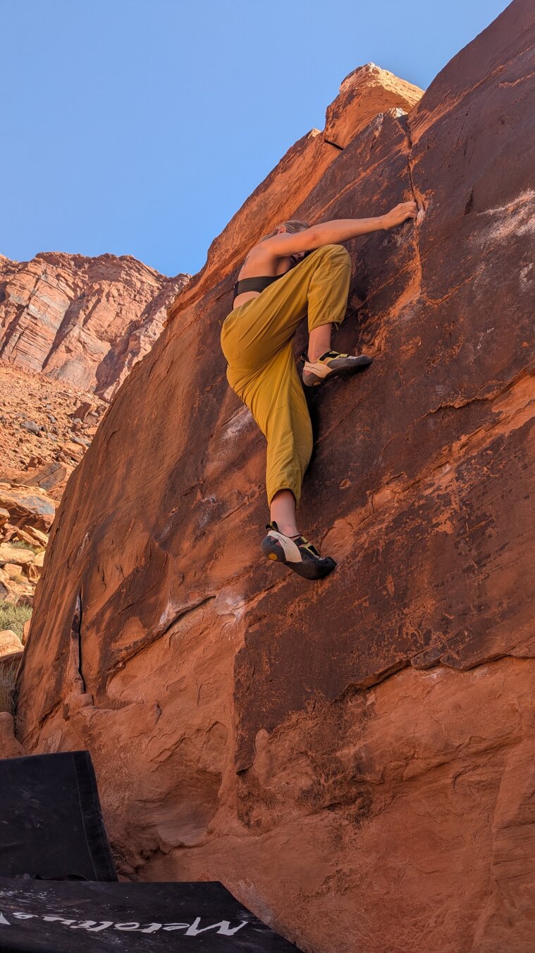 View from below of a climber on a red boulder.