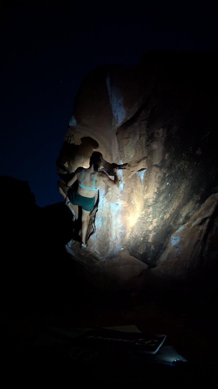 A climber on the wall at night, wearing a headlamp.