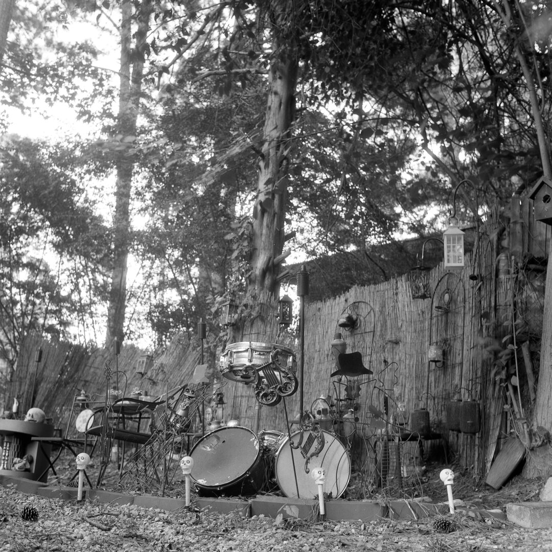 odd sundry decorations in a yard: little plastic skills, lyres, tiki torches, chairs; pinecones in foreground