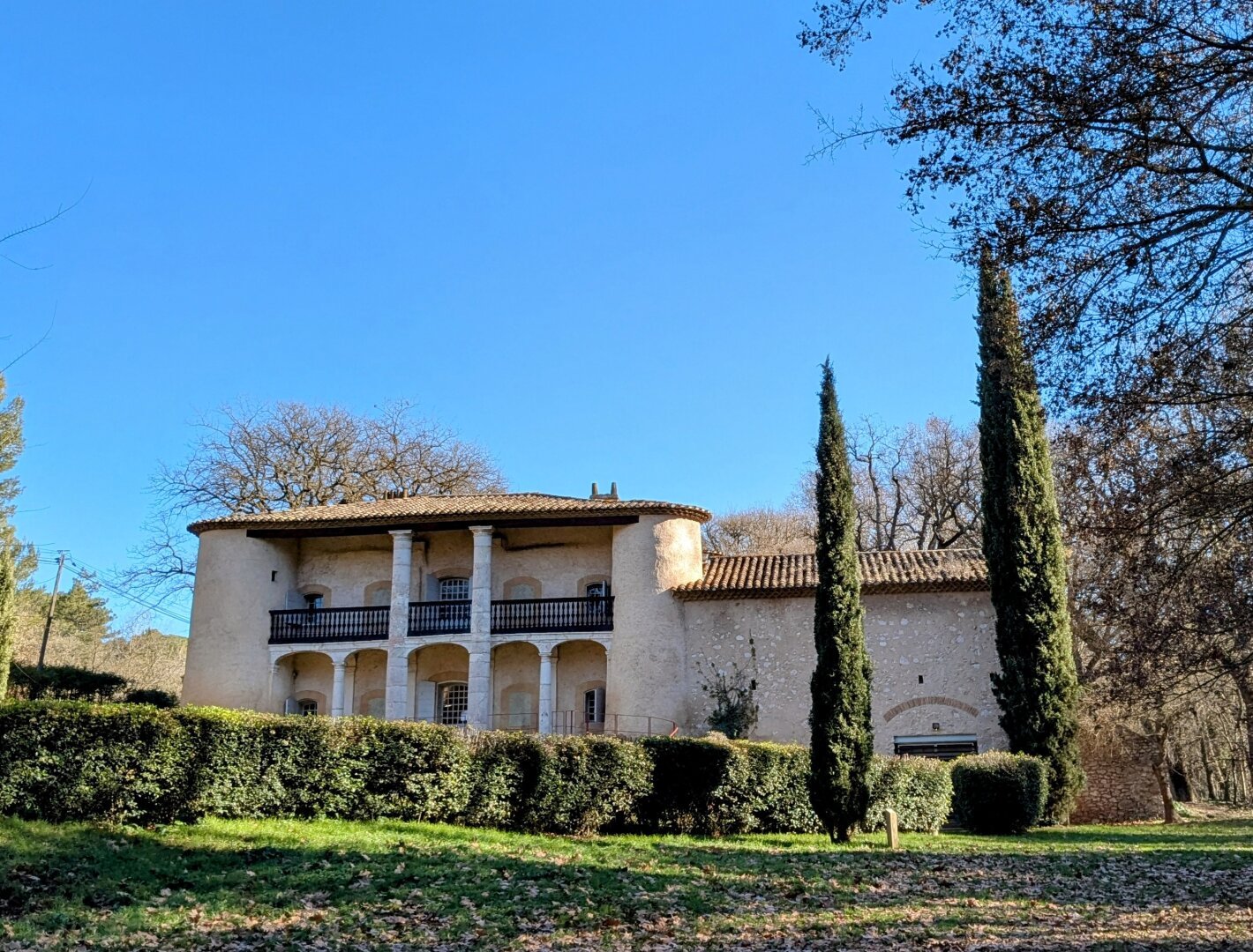 Batisse provençale sous un ciel bleu d'hiver avec de grands platanes autour.