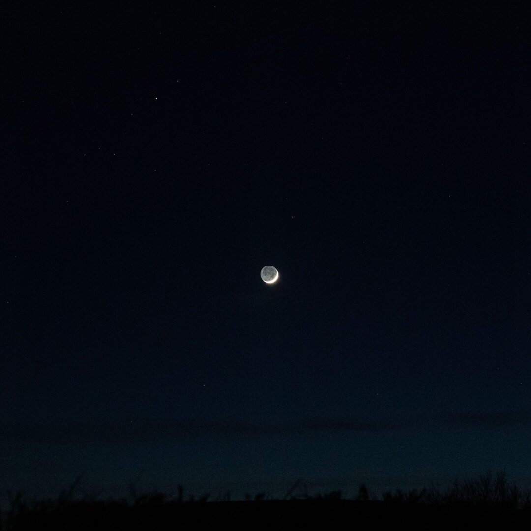 A crescent moon, with the dark part of the moon somehow also visible. A dot of a planet is visible at the top left