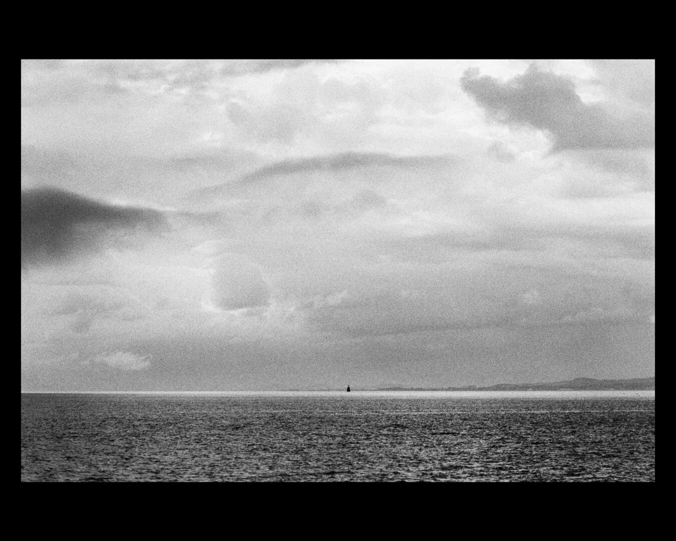 Black and white photo of the ocean, with a single buoy visible in the far distance