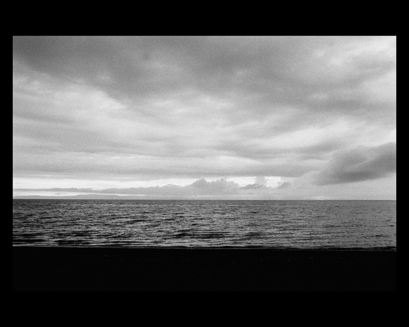 Black and white photo of the ocean with low lying clouds over it