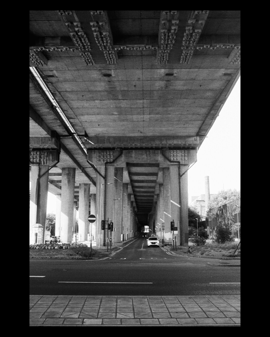 A black and white photo of a road underneath a raised motorway in Glasgow