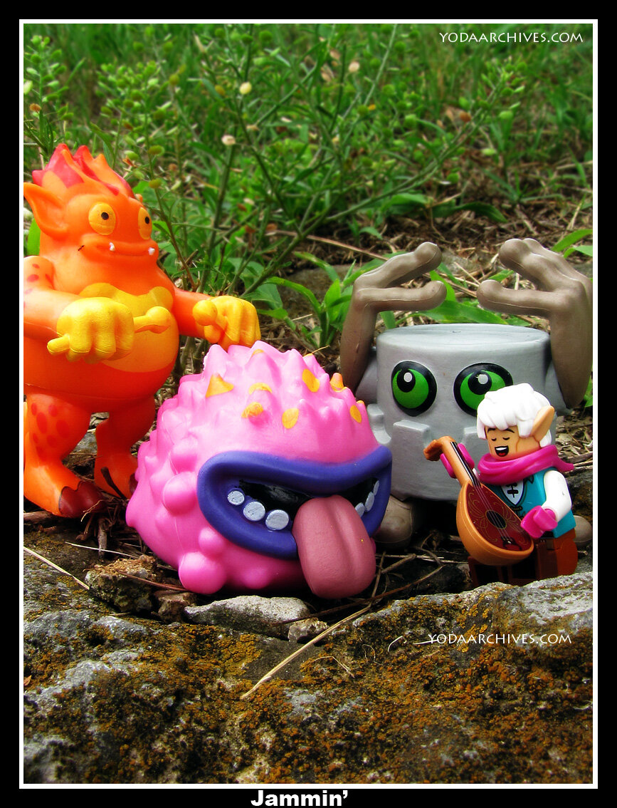 Large orange lizard creature playing drums on his stomach. Pink ball with large mouth singing.  Lego bard with lute.