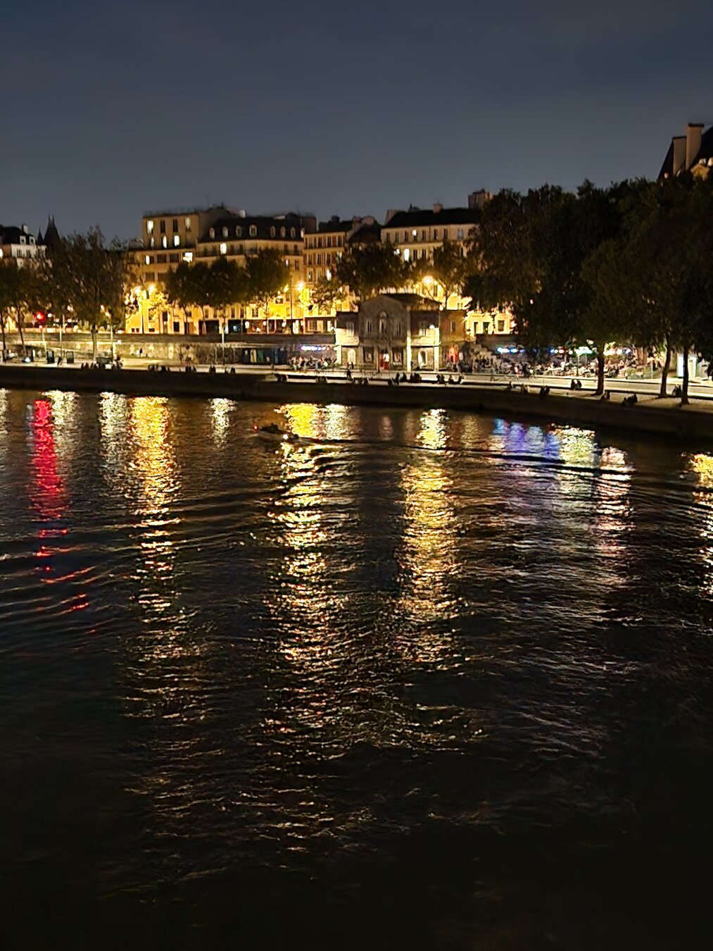 Surface wake of a small boat nearby Pont de Sully in the Seine at night. City lights reflected on the river.
