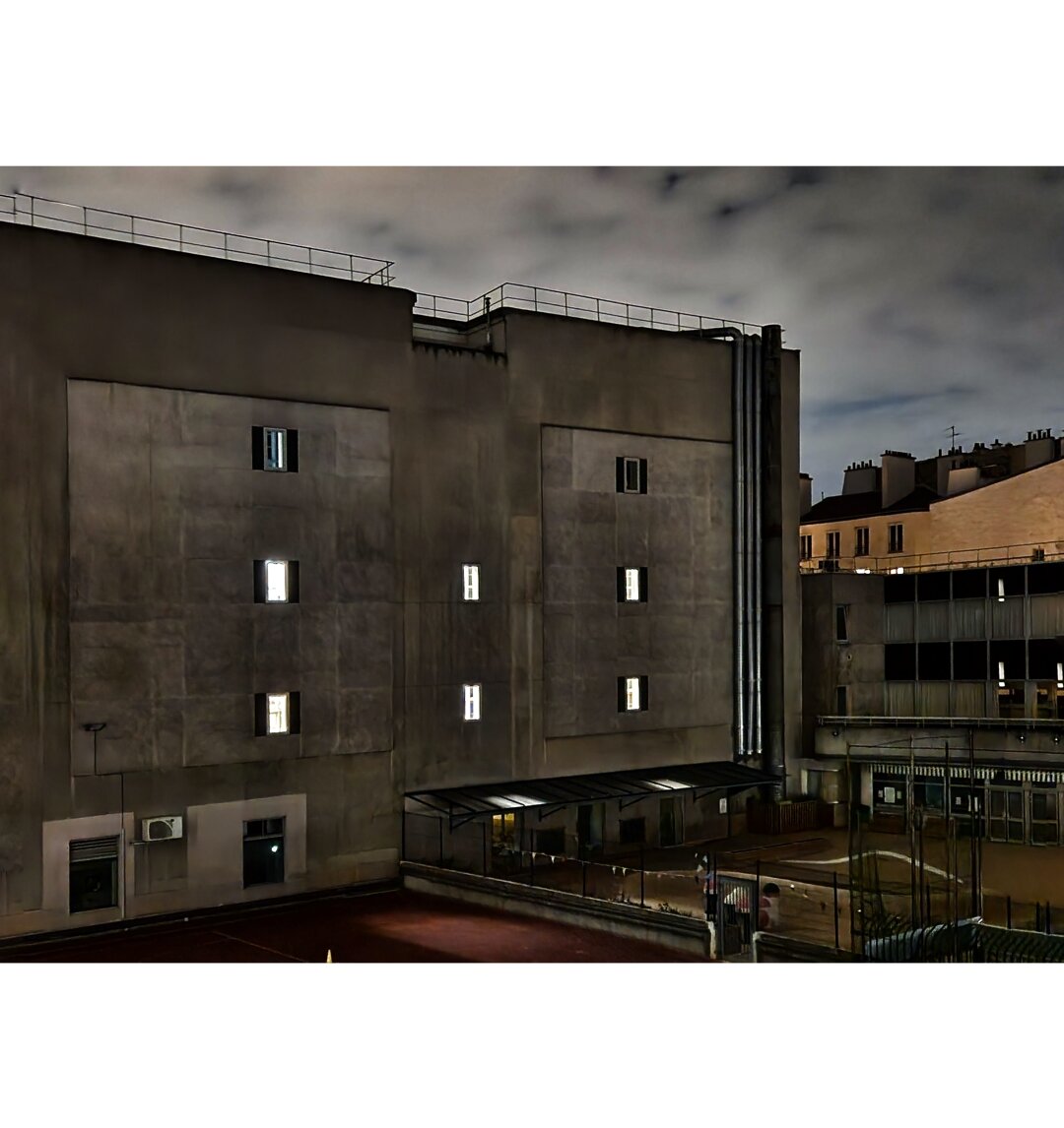 Back of a building with six lit windows. Cloudy sky behind.