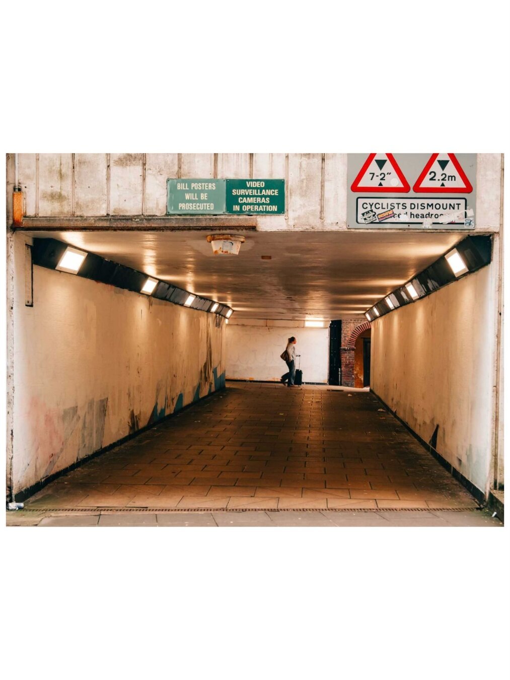Person wheeling a suitcase at the end of an underpass