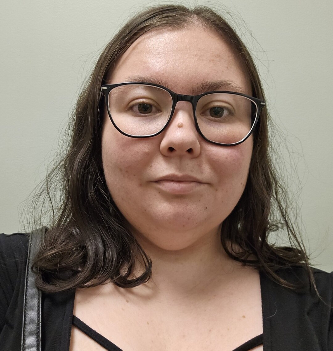 Selfie of woman wearing glasses in black shirt with purse strap on shoulder