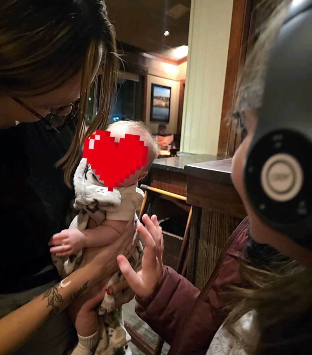 Woman showing baby to little girl wearing black over ear headphones