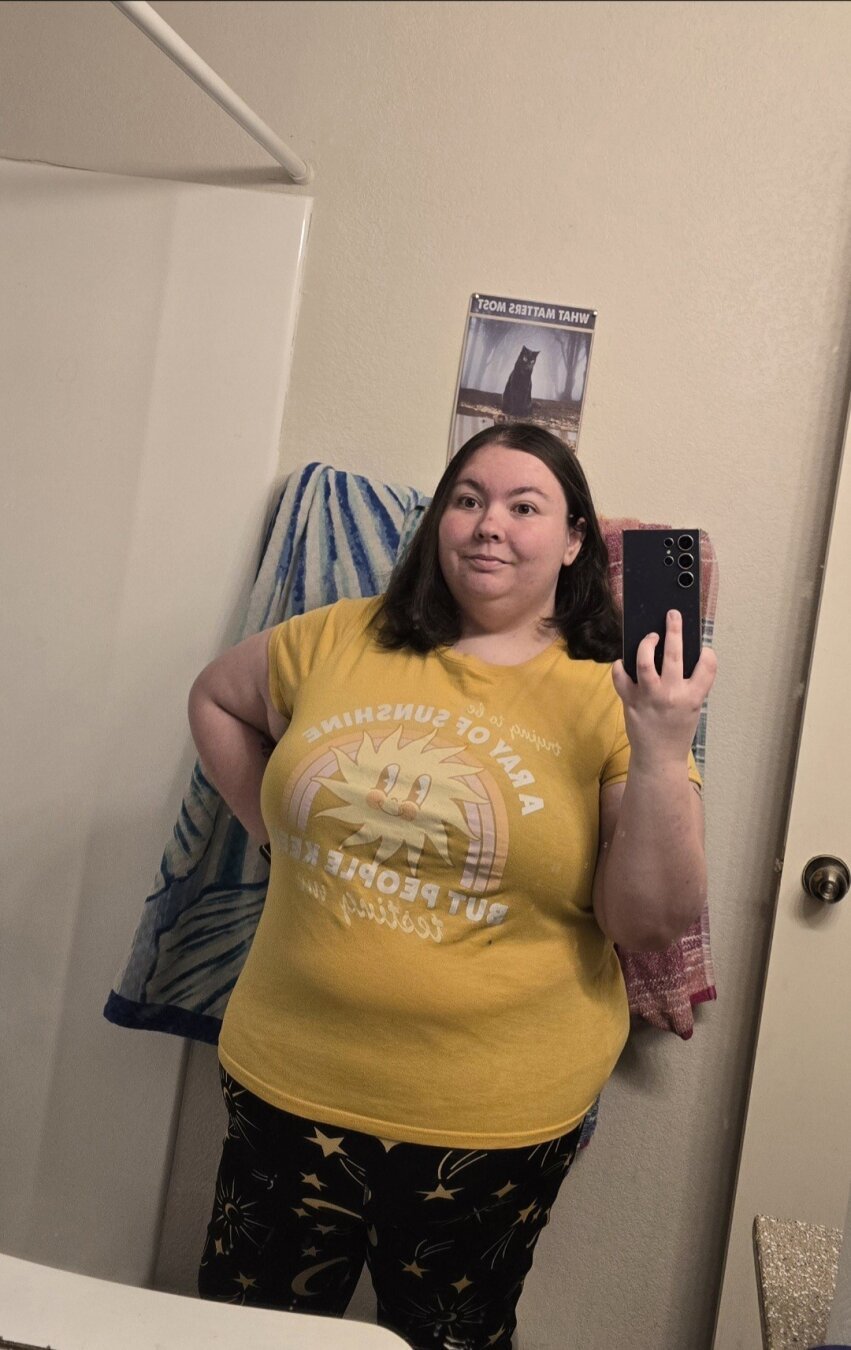 Woman wearing yellow crop top t-shirt with sun and rainbow that says "trying to be a ray of sunshine, but people keep testing me"