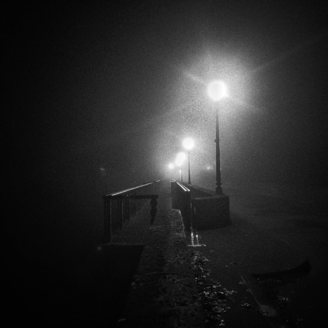 a line of lampposts on a bridge at night. a bit of fog