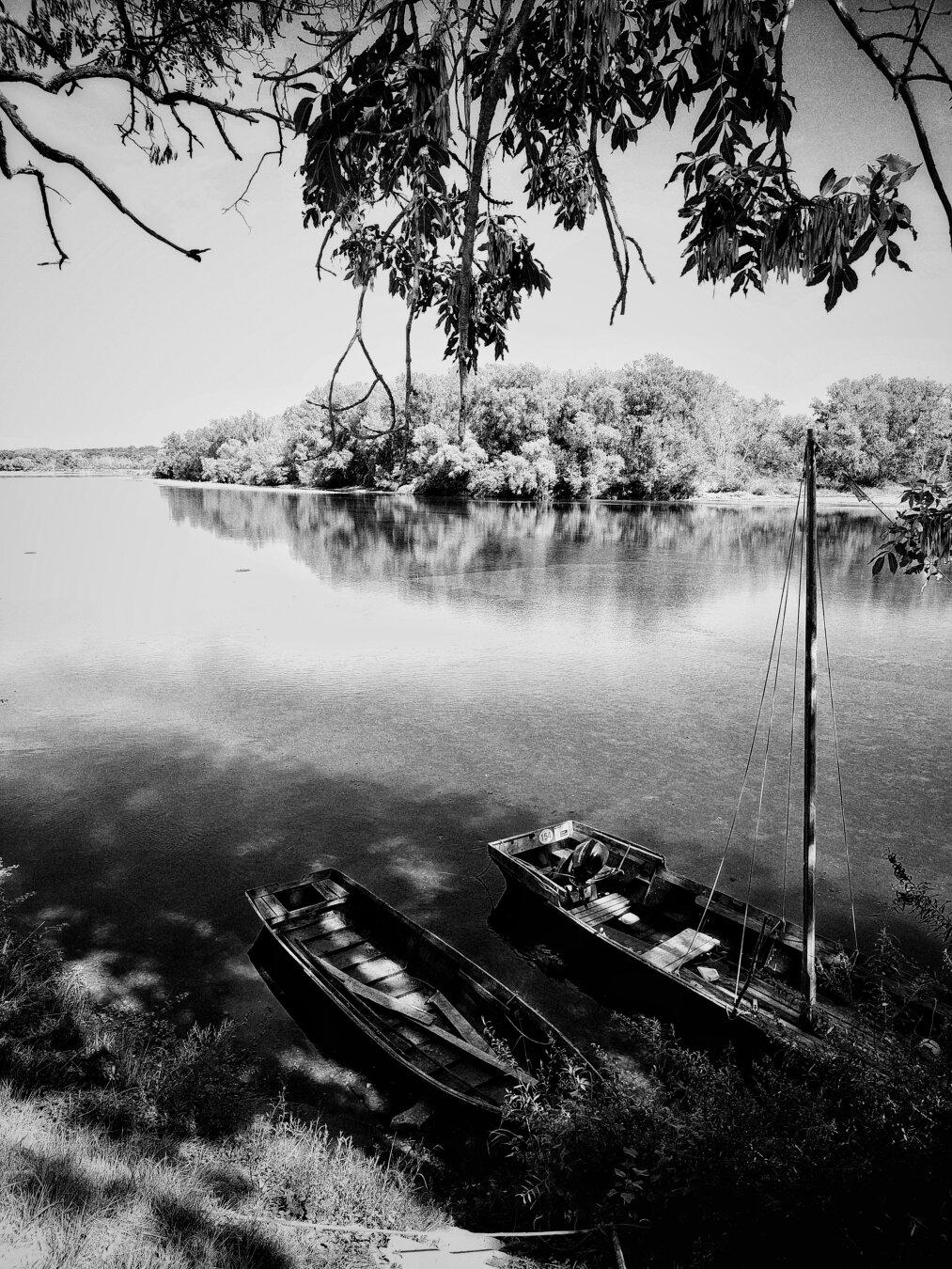 two boats on a river, the sky is burned. there are laods of texture in the river. the boats are in the shadow.