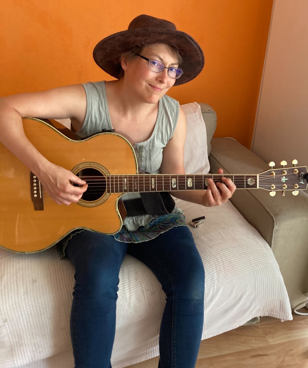 Me wearing an Indiana Jones hat and sitting on the sofa playing guitar.